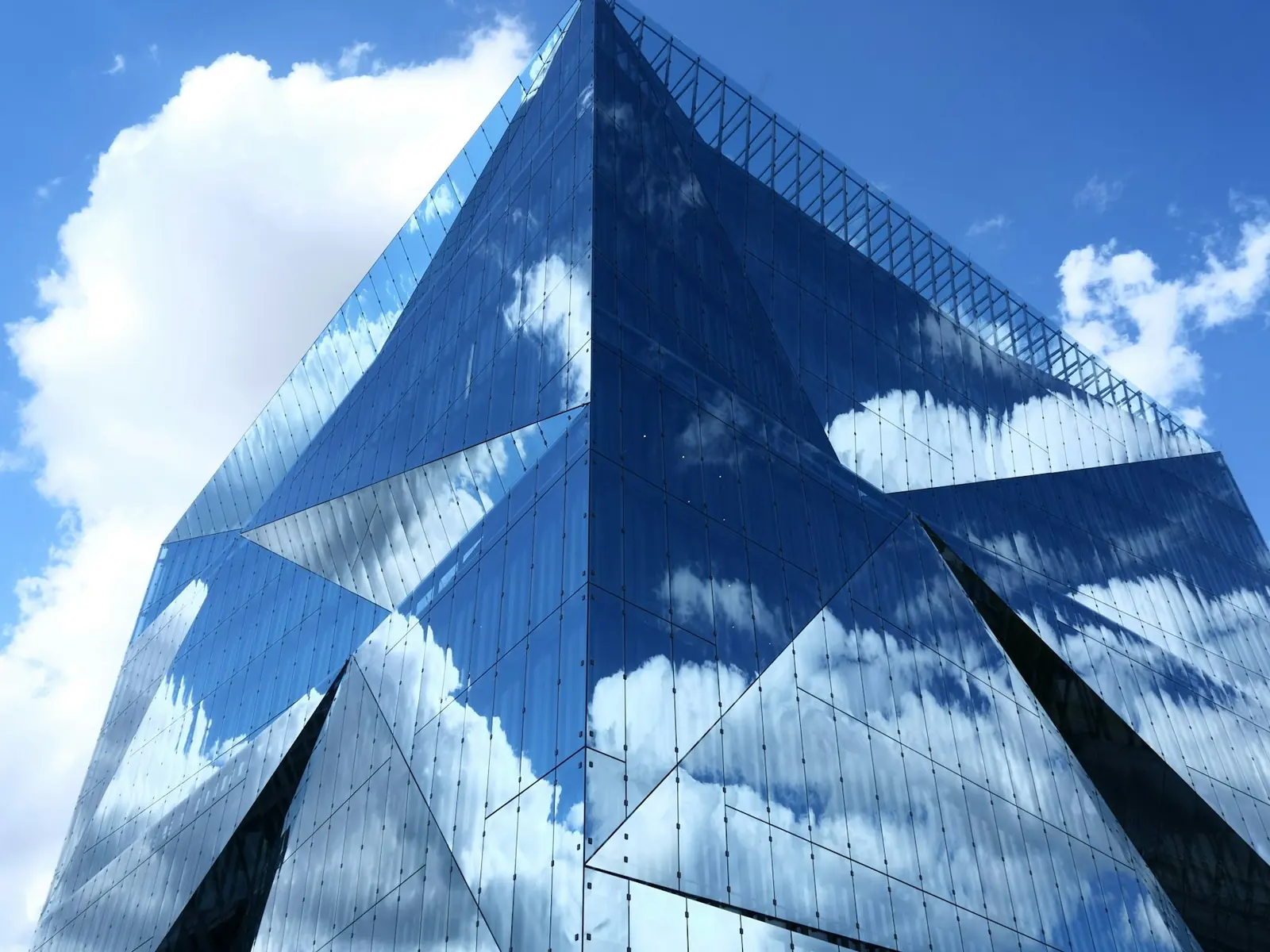 A faceted glass building reflecting blue sky and clouds.